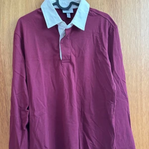 Vinröd pikétröja från H&M - Snygg vinröd långärmad pikétröja från H&M med vit krage och knäppning framtill. Regular fit och tillverkad i mjuk bomull. Perfekt för dig som gillar en klassisk men ändå chill stil.