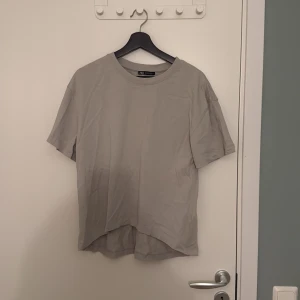 Beige t-shirt från Zara i bomull - Enkel och stilren beige t-shirt från Zara i mjuk bomull. T-shirten har rund halsringning, korta ärmar och en något längre bakdel för en avslappnad vibe. Perfekt för dig som gillar minimalistisk stil.