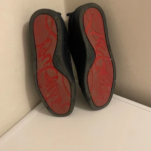 Svarta mockasneakers från Louboutin - Snygga svarta sneakers i mocka från Christian Louboutin med klassisk röd sula och diskret logga undertill. Skorna har svarta snören, rund tå och svart yttersula. Insidan är beige och ger en lyxig känsla. Perfekta för dig som gillar stilrena och exklusiva sneakers. Använt 4 gånger sedan köpt, säljer pågrund av opassande stil. DU FÅR MED ÄVEN KVITTO OCH BOXEN