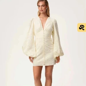 Ljus gul klänning med puffärmar - Superfin vit kort klänning med djup v-ringning och stora puffärmar. Klänningen har knappar framtill och markerad midja som ger en snygg siluett. Perfekt för dig som vill sticka ut med en romantisk och trendig look.