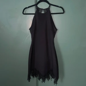 Svart kort klänning med spetsdetaljer - Supersnygg svart kort klänning från NLY Trend med halterneck och spetsdetaljer längs ryggen och nederkanten. Klänningen har en tight passform och är ärmlös, perfekt för dig som vill sticka ut med en elegant och stilren look. Använd en gång.