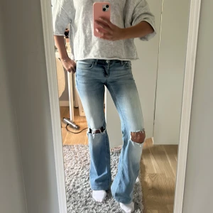 Ljusblå bootcut jeans med slitningar - Säljer ett par ljusblå bootcut jeans med slitna knän och snygg tvätt. Jeansen har klassiska bakfickor med lock och knapp, samt low waist.