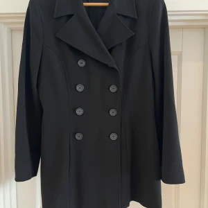 Svart dubbelknäppt skepparkavaj Twist & Tango - Stilren svart skepparkavaj med dubbelknäppning och bred krage. Jackan har långa ärmar och är helfodrad på insidan. Klassisk modell som ger en clean och tidlös look. Perfekt för dig som gillar minimalistisk stil. Har för mig att det är stl 38 men en ganska stor 38..så funkar som liten stl 40