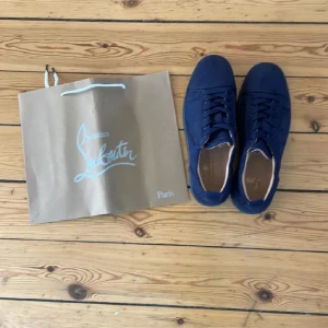 Blå sneakers från Christian Louboutin - Snygga blå sneakers från Christian Louboutin med klassisk röd sula och diskret logga på insidan. Skorna har rund tå, snörning och är tillverkade i mocka för en lyxig känsla. Perfekta för dig som vill sticka ut med exklusiva detaljer. Aldrig använda 