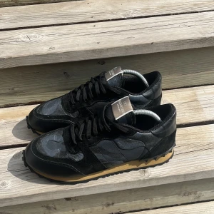 Valentino Garavani Rockrunner sneakers - Snygga svarta Valentino Garavani Rockrunner sneakers med camouflagemönster. Skorna har ovandel i skinn och mocka, svarta snören och en beige sula med coola nitar baktill. Bra skick passar även 41