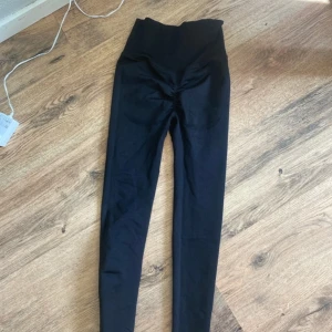 Svarta scrunch leggings från Nebbia - Säljer ett par svarta leggings från Nebbia med scrunch-detalj bak och hög midja. De är tighta och har en diskret logga på höften. Perfekta för gymmet eller chill dagar. Materialet är stretchigt och följsamt.