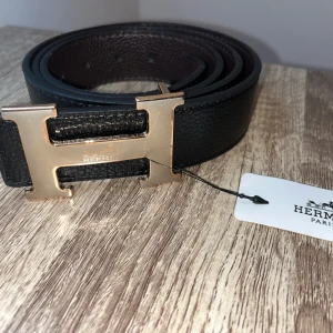 Svart bälte med ett H - Längd: 120cm