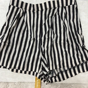 Randiga shorts från H&M, strl 34 - Svartvita shorts från H&M i storlek 34 med vertikala ränder. De har elastisk midja baktill och är tillverkade i mjuk viskos som känns skön mot huden. Perfekta för varma dagar när du vill ha en chill och snygg look. Dom är luftiga och var fickor. 