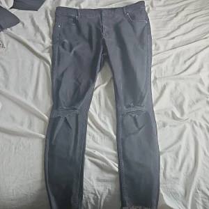 Svarta skinny jeans från H&M - Svarta skinny jeans från H&M i storlek 48/50. Byxorna har slitna detaljer vid knäna och fransad nederkant för en edgy look. Klassisk femficksmodell med dragkedja och knapp. Perfekta för dig som gillar en smal passform och streetstil.