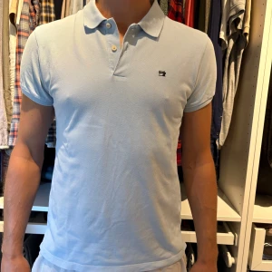 Ljusblå piké från Scotch & Soda - Säljer en ljusblå pikétröja med klassisk krage och två knappar framtill. Tröjan har korta ärmar och en liten broderad logga på bröstet. Perfekt för en clean och stilren look. Nypris 699