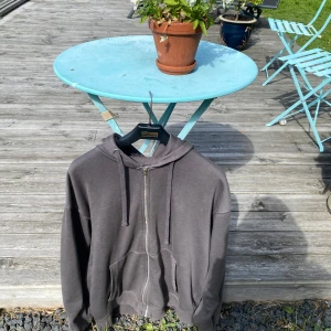 Mörkgrå hoodie med dragkedja från Bershka - Säljer en mörkgrå hoodie från Bershka med dragkedja framtill, huva med snörning och två stora fickor. Oversized passform och mjukt material som känns skönt mot huden. Perfekt för chill dagar eller när du vill ha en enkel streetstyle-look.