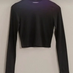 Svart croppad långärmad topp Vogue - En svart, croppad långärmad topp från Vogue Collection. Enkel och stilren design med rund halsringning och tight passform. Perfekt att matcha med höga jeans eller kjol för en clean look.