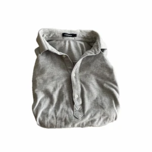 Grå henley från J.Lindeberg - Snygg grå henley från J.Lindeberg med klassisk krage och knappar framtill. Skjortan är långärmad och tillverkad i mjuk bomull, perfekt för en clean och avslappnad stil.