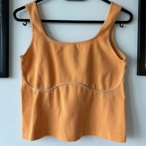 Ribbad orange linnetopp - Snygg ribbad linnetopp i en mjuk orange färg med breda axelband och markerad söm under bysten. Toppen har en croppad passform men går ner till midjan till mig som är 173.