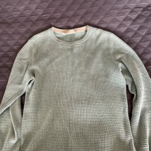 Turkos stickad tröja med struktur - Snygg turkos stickad tröja med lång ärm och rund hals. Tröjan har ett strukturerat rutmönster och ribbade muddar vid ärmslut och nederkant. Perfekt för dig som gillar en enkel men ändå unik stil.