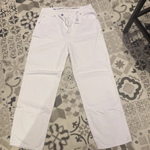 Vita straight jeans från Never Denim - Säljer ett par fräscha vita jeans från Never Denim i modellen 90s Straight. Byxorna har hög midja, raka ben och klassisk femficksdesign. Materialet är jeans och de har en snygg läderpatch bak i midjan. Perfekta för dig som gillar en clean och stilren look. Helt oanvända nypris 599 