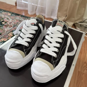 Maison Mihara Yasuhiro svarta sneakers - Unika svarta sneakers från Maison Mihara Yasuhiro med chunky vit sula och kontrasterande vita sömmar. Skorna har breda vita snören, rund tå och detaljer i beige vid tån. Skorna är stor i storlek. Pris kan diskuteras vid snabb affär