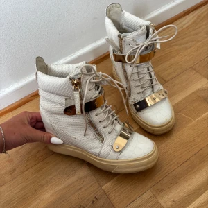 Giuseppe Zanotti kilklack skor - Giuseppe Zanotti skor, Skorna är vita med guld detaljer de är även kilklack. De är andvända i gott skick små slitningar men ingen större defekt. Storlek 35 men sitter mer som 36/37