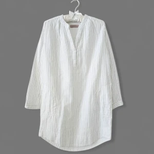 Vit randig henley i bomull - Vit henley-skjorta klänning från NOA NOA med tunna svarta ränder. Har v-ringad hals utan knappar, lång ärm och avslappnad passform. Tillverkad i mjuk bomull, perfekt för en chill och stilren look.