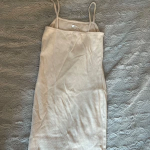Beige ribbad klänning från Amisu - Snygg beige ribbad klänning från Amisu i storlek 38. Klänningen är ärmlös med smala axelband och har en kroppsnära passform. Perfekt för dig som gillar en enkel och stilren look med en touch av sommarvibe. Tar även fram dina kurvor!