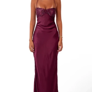 Vinröd maxiklänning med paljetter - Supersnygg populär vinröd maxiklänning i satinliknande material med smala axelband och öppen rygg med snörning. Överdelen är dekorerad med glittriga paljetter som ger extra wow-känsla. Perfekt inför balen eller något fest. Den är endast använd en gång och är i helt nyskick. Den är från märket ”I Am Delilah” och är helt slutsåld. 