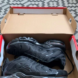 Nike Air Max Plus All Black EUR 39 - Nike Air Max Plus i helsvart med mesh och syntetiska paneler, ikoniska vågformade detaljer och synlig Air Max-dämpning i sulan. Snygg och sportig siluett med svarta snören och diskret Swoosh-logga på sidan. Perfekt för dig som gillar streetstyle.