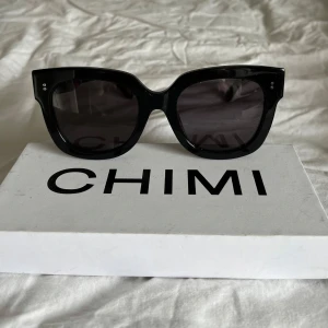 Svarta solglasögon CHIMI #008 - Snygga svarta solglasögon från CHIMI, modell #008 Berry. De har en kraftig båge i blank svart plast och mörka glas. Perfekt accessoar för att lyfta din stil och skydda ögonen mot solen. Kommer med originalbox samt dustbag.
