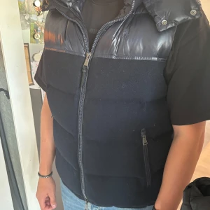 Svart dunväst med huva från Polo Ralph Lauren - Snygg svart dunväst från Polo Ralph Lauren med stor vadderad huva och dragkedja framtill. Har använt den fåtalet gånger. Den är lite nopprig men annars väldigt bra skick. 