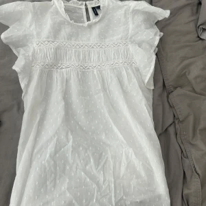 Vit blus från Vero Moda XS - Supersöt vit blus från Vero Moda i tunn bomull med diskret prickigt mönster, volangärmar och spetsdetaljer över bröstet.
