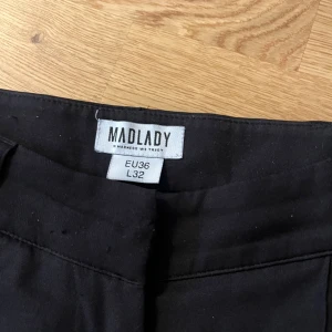 Svarta kostymbyxor från Madlady - Svarta kostymbyxor från Madlady i klassisk rak modell med pressveck framtill. Byxorna har hög midja och vida ben, vilket ger en snygg och stilren look. Perfekta att matcha med en crop top eller oversized skjorta.
