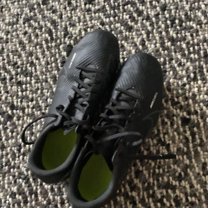 Nike Mercurial svarta fotbollsskor - Säljer ett par svarta Nike Mercurial fotbollsskor med snörning och gula dobbar. Skorna har en sportig design med diskreta silverdetaljer och är tillverkade i syntetmaterial för bästa grepp på planen. Perfekta för dig som vill ha stilrena och snabba skor till matchen.
