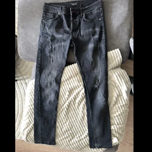 Svarta Philipp Plein jeans straight fit - Svarta jeans från Philipp Plein i straight fit med slitna detaljer och klassisk femficksdesign. Byxorna är tillverkade i 99% bomull och 1% lycra för en skön stretch. Snyggt diskret märke på fickan och röd detalj vid gylfen.