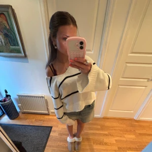 Vit stickad randig hoodie - Vit stickad hoodie med svarta horisontella ränder och huva. Tröjan har en oversized passform, långa ärmar och breda muddar. Perfekt för en chill och avslappnad stil.