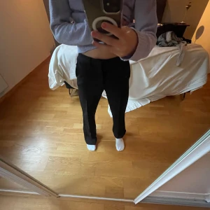 Svarta kostymbyxor från Kappahl - Snygga svarta kostymbyxor från Kappahl i rak modell. Byxorna har medel midja och klassisk passform med pressveck framtill. Perfekta till en stilren look och passar till många olika outfits. Använda fåtal gånger. JAG ÄR 160 CM LÅNG!!