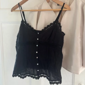 Svart spetslinnetopp från Zara - Supersöt svart linnetopp från Zara med tunna axelband, knappar framtill och fina spetsdetaljer längs kanterna. Använd 1 gång🥰