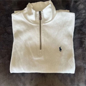 Polo Ralph Lauren vit half zip - Vit långärmad tröja från Polo Ralph Lauren med half zip och klassisk broderad logga på bröstet. Tröjan är i bomull och har en stilren, enkel design med hög krage. Perfekt för dig som gillar en clean och tidlös look.