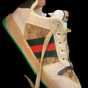  sneakers mönstade och gröna sulor - Snygga sneakers i beige och brunt med klassiskt mönster, gröna och röda ränder på sidan och grön sula med bi-detalj undertill. Skorna har snörning, detaljer i skinn och textil samt rund tå. Perfekt för dig som vill sticka ut med lyxig streetstyle.kvitto Finn’s ny pris 13400