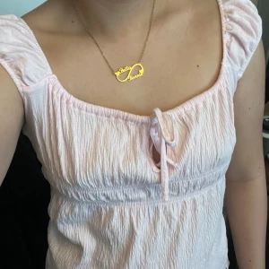 Ljusrosa blus med knyt fram lager 157 - Supersöt ljusrosa blus med puffiga korta ärmar och knyt fram. Blusen har en rynkad struktur och en luftig, somrig känsla. Perfekt för dig som gillar romantisk och feminin stil.