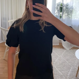 Svart topp med puffärmar - En svart topp med rund hals och korta puffärmar. Lite strukturerat material. Storlek XS men passar även S. 
