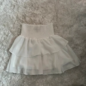 Vit volangkjol från Chelsea XS - Supersöt vit kortkjol från Chelsea med bred smock i midjan och dubbla volanger, perfekt för varma dagar. Kjolen är i bra skick