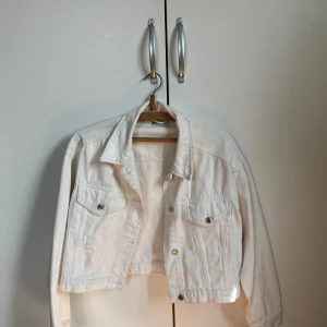 Vit croppad jeansjacka - Snygg vit croppad jeansjacka med klassisk krage och två bröstfickor med knappar. Jackan har långa ärmar och silverfärgade knappar framtill.  Använd 2-3 gånger, inköpt från Gina tricot