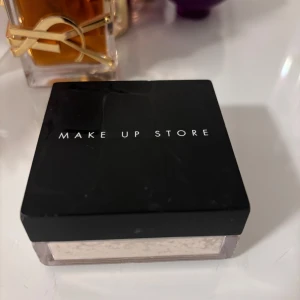 Make Up Store transparent puder - Säljer ett transparent löspuder från Make Up Store i en stilren fyrkantig burk med svart lock. Perfekt för att fixera sminket och ge en matt finish. Passar alla hudtoner och ger en naturlig look.