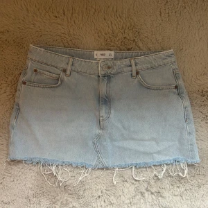 Ljusblå jeanskjol  - En ljusblå jeanskjol från MANGO i storlek L. På baksidan finns det lite missfärgning för lappen suttit (titta bild) men annars inga tydliga tecken på användning. Rakt över midjemått:40cm.