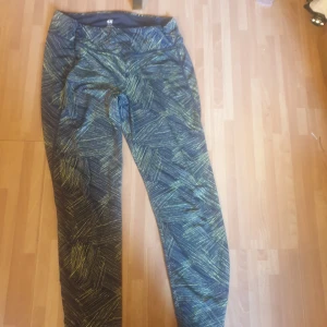 Mönstrade träningstights från H&M Sport - Säljer ett par svarta och gröna träningstights från H&M Sport i storlek M. De har ett coolt grafiskt mönster och är gjorda i stretchigt syntetmaterial som sitter tight och bekvämt. Perfekta för gymmet eller löprundan.