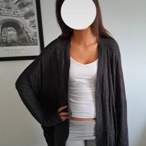 Mörkgrå loose kofta från L.O.G.G. - Mysig mörkgrå kofta från L.O.G.G. i loose fit. Koftan är öppen framtill, har långa ärmar och är tillverkad i ett mjukt, tunt material som känns skönt mot huden. Perfekt att slänga på sig över ett linne eller t-shirt för en chill look.