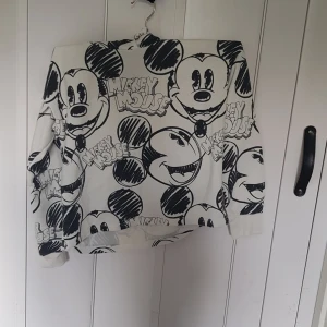 Vit Mickey Mouse hoodie från H&M - Supercool vit hoodie från H&M med stora svarta Mickey Mouse-tryck över hela tröjan. Långärmad modell med huva och mjukt material som är perfekt för chill dagar. Disney-logga på insidan. Perfekt för dig som älskar tecknade motiv!