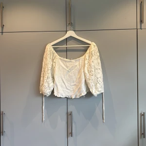 Vit spetsig bolerotopp  - Superfin vit bolerotopp från FB Sister med puffiga spetsärmar och blommigt mönster. Toppen är croppad, har offshoulder-modell och smockad kropp. Perfekt för dig som gillar romantiska vibes och snygga detaljer. ❣️❣️ Strl L!!❣️❣️
