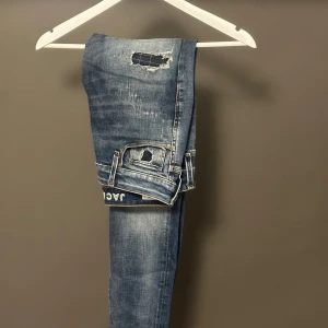 Slim fit jeans från Jack & Jones - Snygga blå slim fit jeans från Jack & Jones, modell Glenn. Jeansen har slitna detaljer och hål på benen för en cool, avslappnad look. Klassisk femficksmodell med normal midja och dragkedjegylf. Perfekta för dig som gillar en smalare passform.