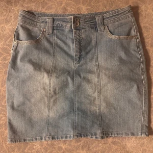 Ljusblå jeanskjol med fickdetaljer - Snygg ljusblå jeanskjol med klassisk femficksdesign och coola silverdetaljer vid fickorna framtill. Kjolen har bälteshällor, dubbla knappar i midjan och en rak, kort passform. Perfekt att matcha med sneakers eller boots.