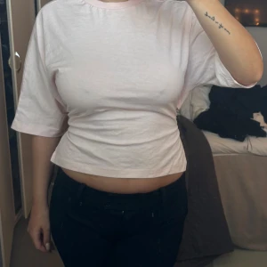 Ljusrosa croppad topp med knyt - Säljer en söt ljusrosa croppad topp med knyt i ryggen. Toppen har korta ärmar och en rund halsringning. Perfekt för en avslappnad stil.